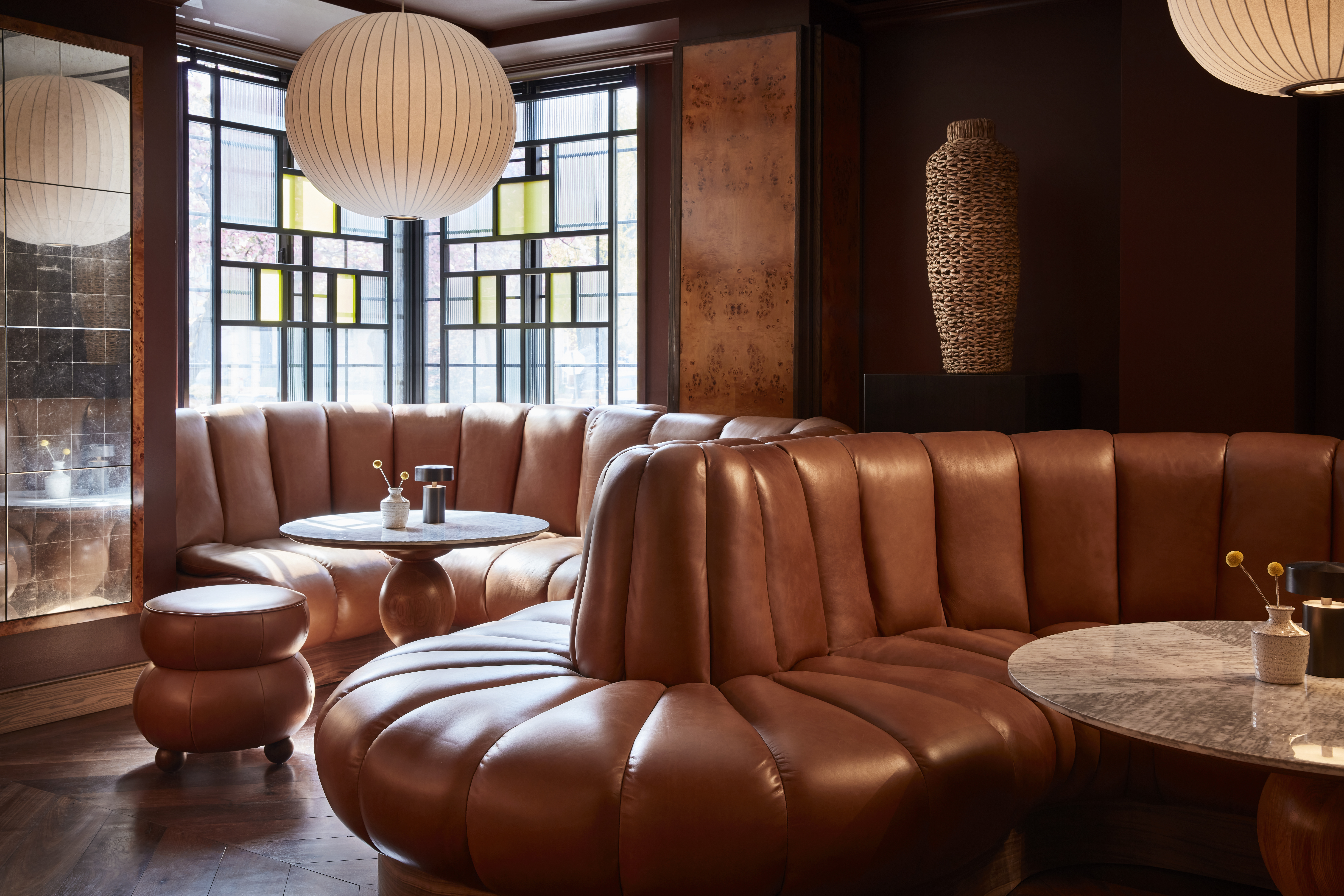 A cozy lounge area with plush brown leather seating, round marble tables, and warm lighting in the Bar at Lyle's DC.