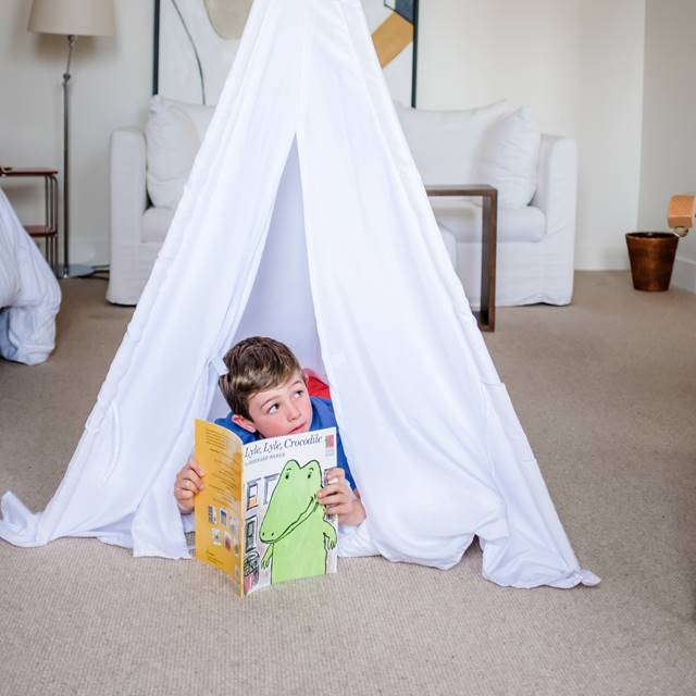 Child reading 'Lyle Lyle Crocodile' in teepee in Lyle guest room.