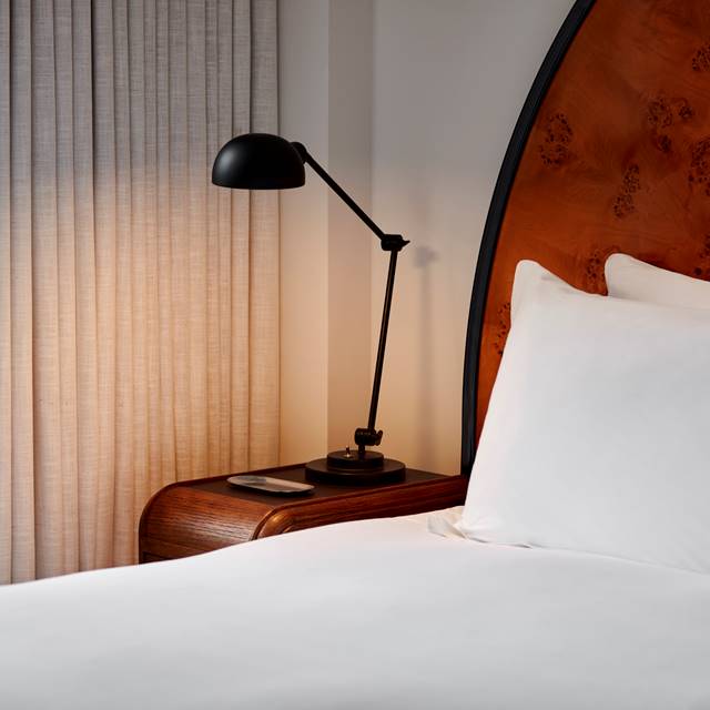 A modern hotel room at Lyle DC with a curved wooden headboard, white bedding, a bedside table, and a black adjustable lamp.
