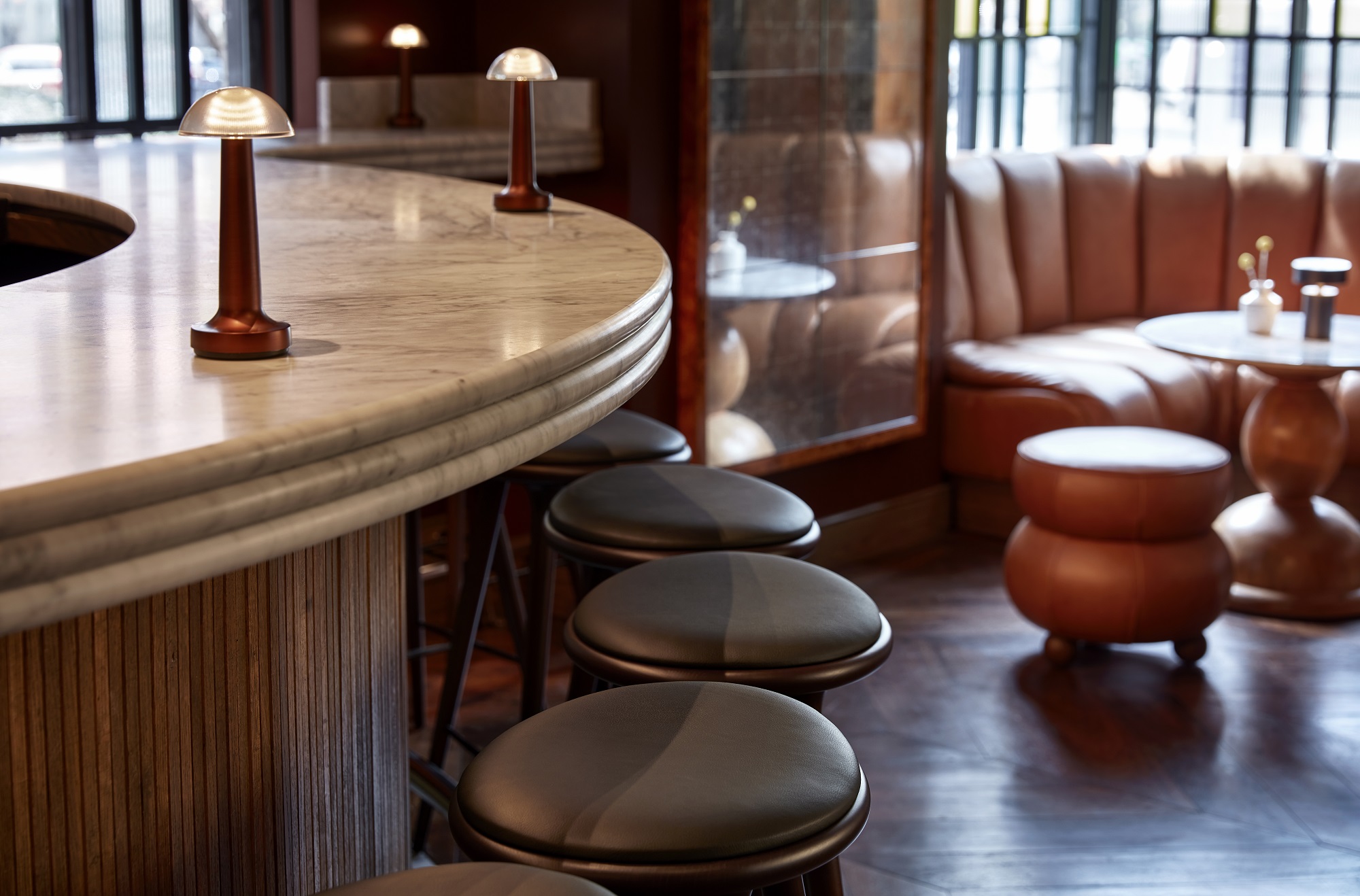 A sleek bar at Lyle's Bar with a curved marble countertop, leather barstools, and warm ambient lighting.