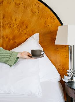 Hand holding a mug in front of burl wood headboard